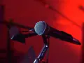 Mikrofon na statywie, gotowy do nagrania nastrojowego utworu w stylu trip hop. Czerwone światło tworzy atmosferę.