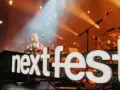 Światła sceny oświetlają napis "next fest" i artystkę grającą na gitarze.