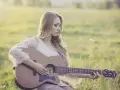 Blondynka w koronkowej sukience gra na gitarze w słonecznym polu. To jak remaster starych wspomnień, pełen ciepła i nostalgii.