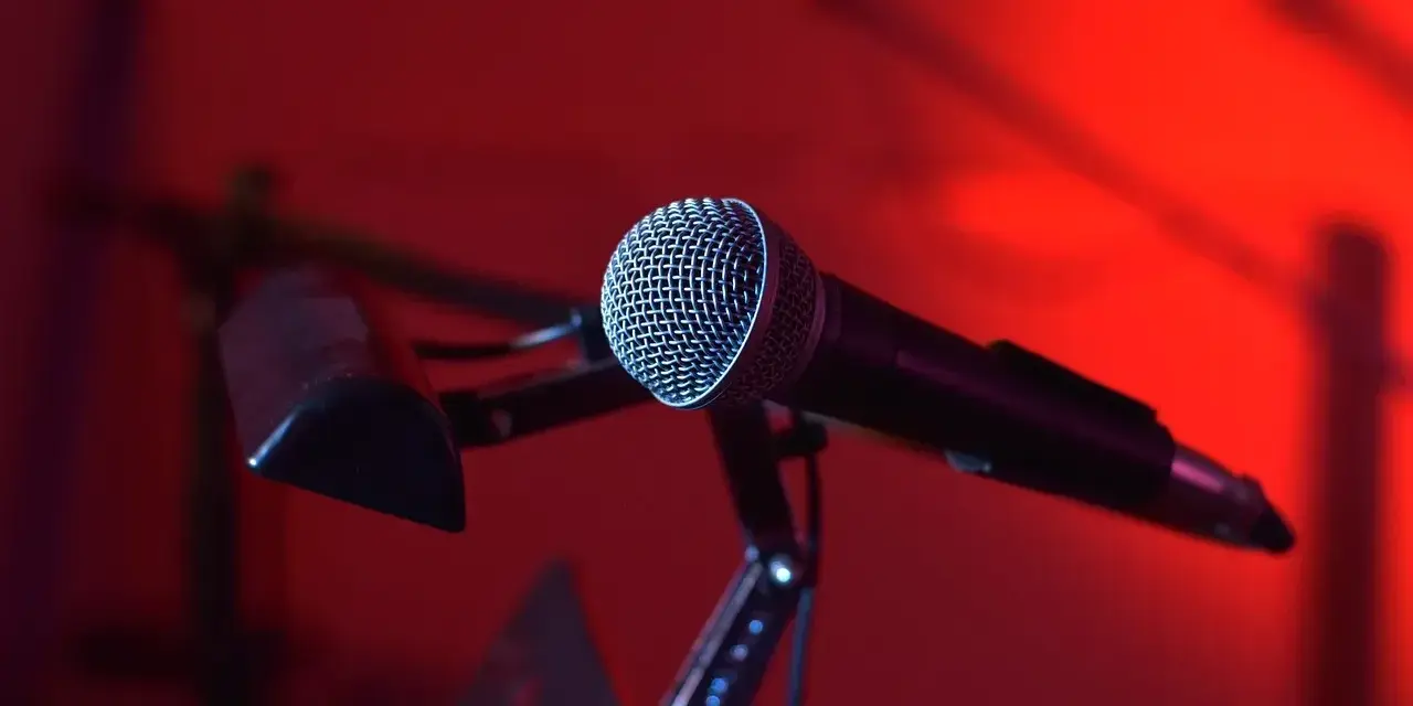 Mikrofon na statywie, gotowy do nagrania nastrojowego utworu w stylu trip hop. Czerwone światło tworzy atmosferę.