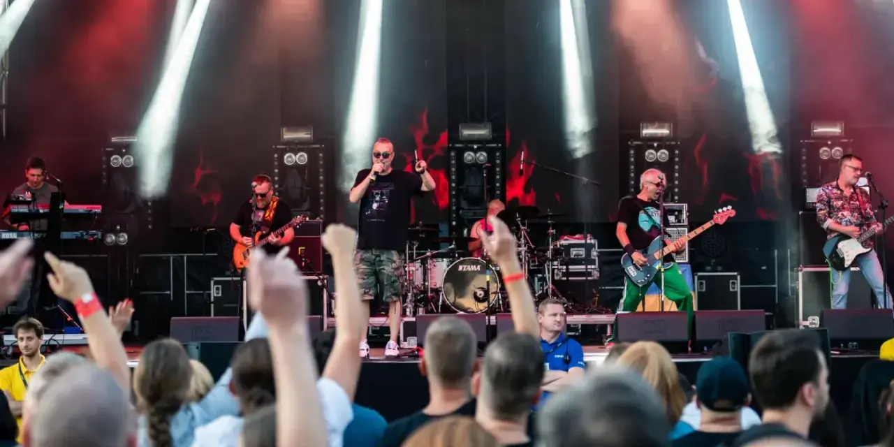 Zespół gra na scenie podczas festiwalu w Jarocinie. Widać publiczność, światła i instrumenty.