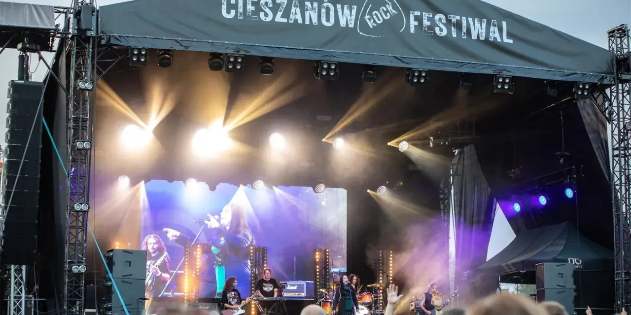 Zespół gra na scenie podczas Cieszanów Rock Festiwal. W tle wielki ekran z wizerunkiem wokalistki i reflektory.