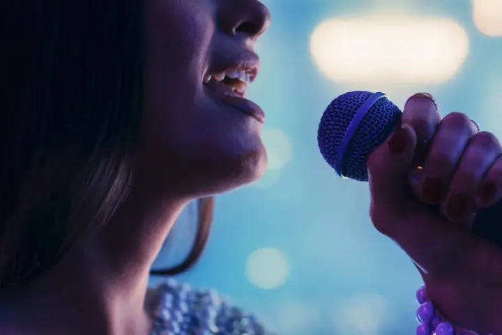 Kobieta śpiewa do mikrofonu. Czy to playback? Wokalistka z błyszczącą suknią i fioletowym mikrofonem.