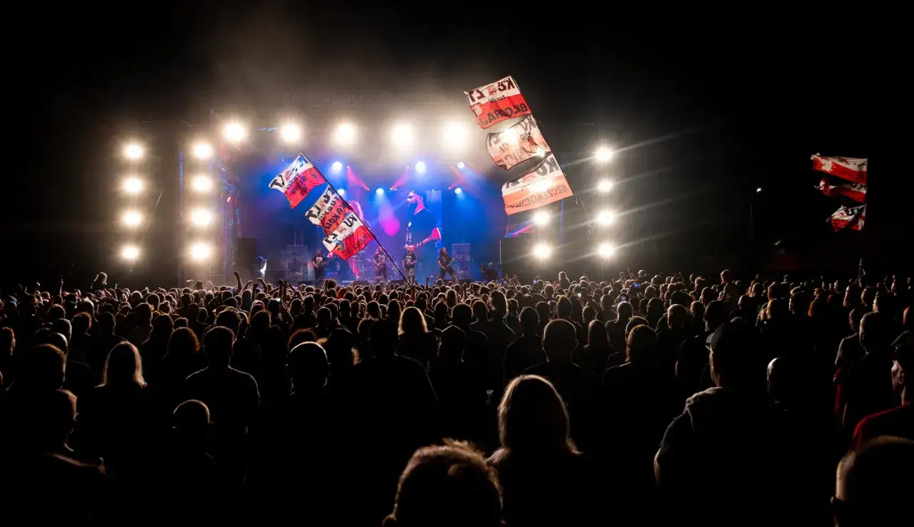 Tłum na Cieszyn Rock Festiwal, z flagami powiewającymi przed sceną oświetloną światłami.