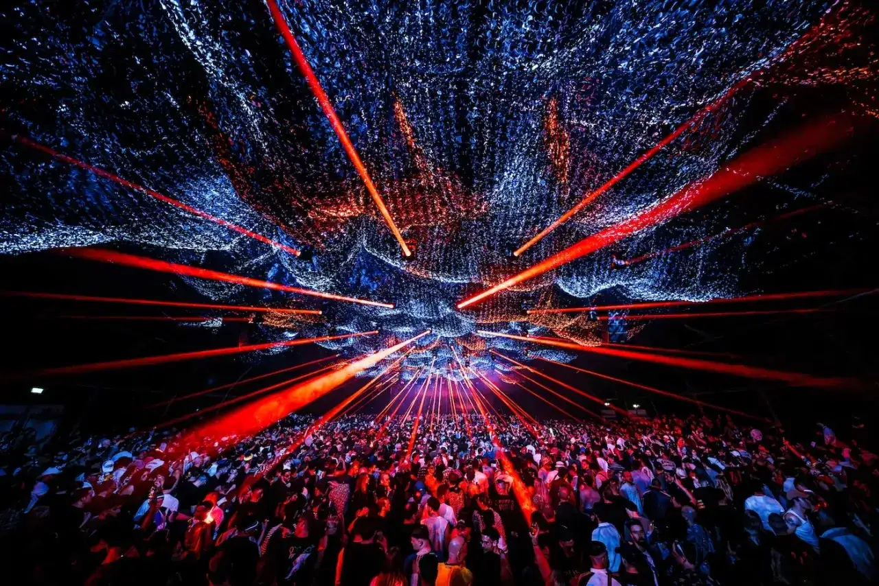 Tłum ludzi tańczy pod czerwonymi laserami i niebieską siatką. To scena z największych imprez techno na świecie.