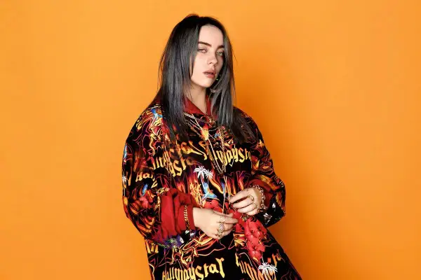 Billie Eilish teraz w kolorowej kurtce z nadrukiem na pomarańczowym tle.