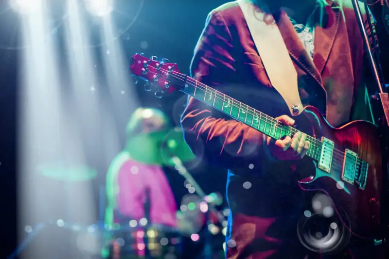Koncertowe emocje! Gitarzysta gra na scenie, a w tle widać perkusistę. To jakby występ znanych zespołów muzycznych zagranicznych.